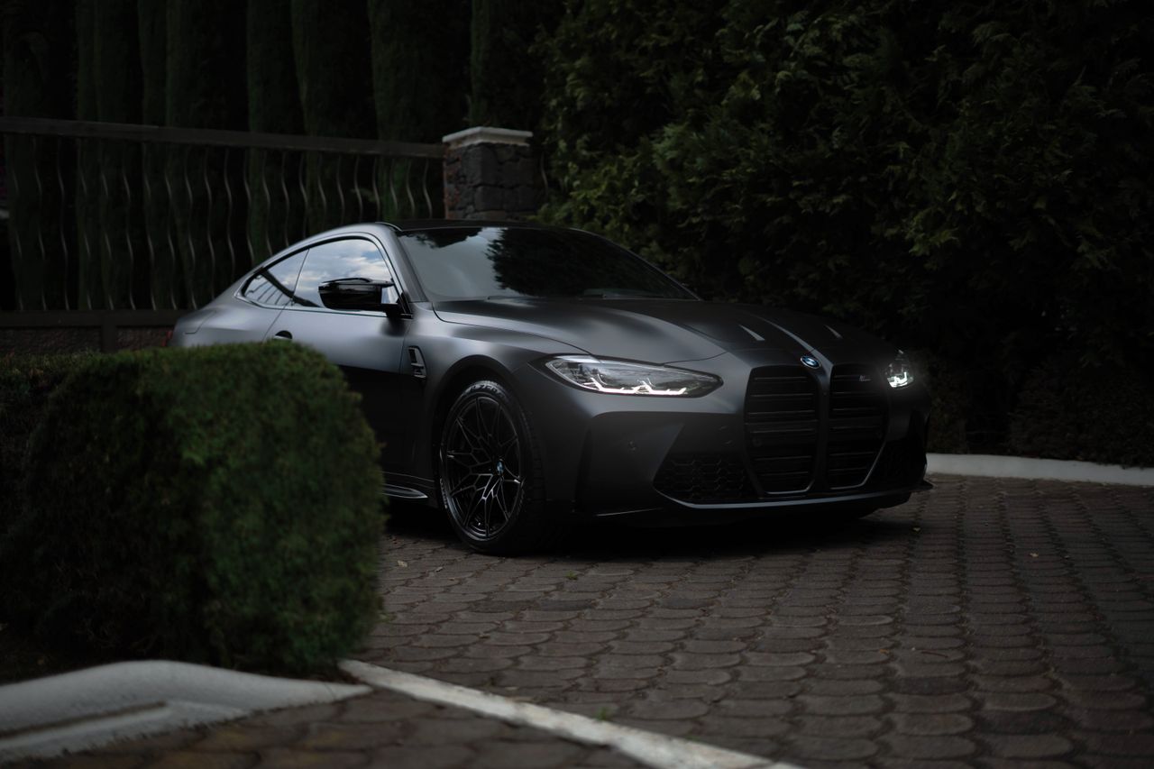 Black sports car parked outdoors on a paved surface with greenery around.