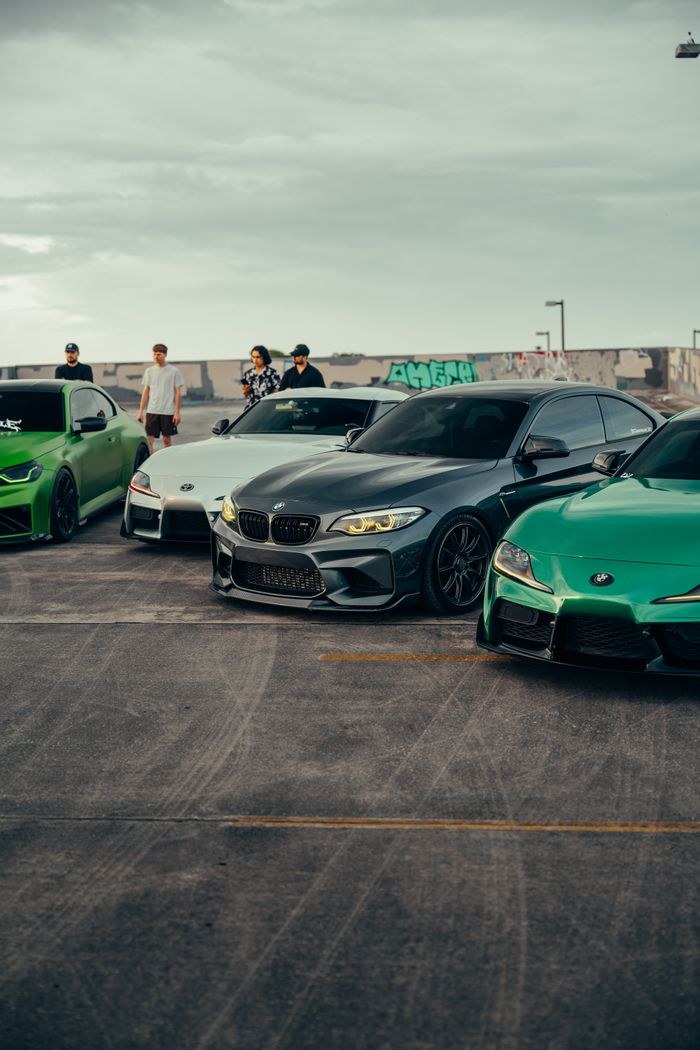 Three vibrant sports cars parked on a rooftop with people capturing the scene, urban graffiti in the background.